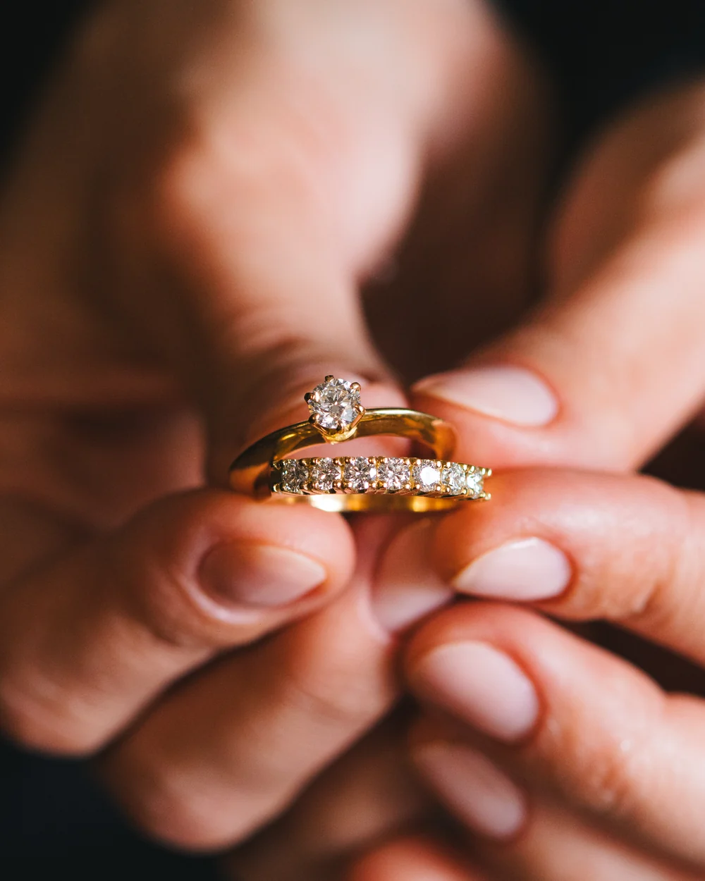 Mãos segurando um solitário e uma meia aliança Halo em ouro amarelo